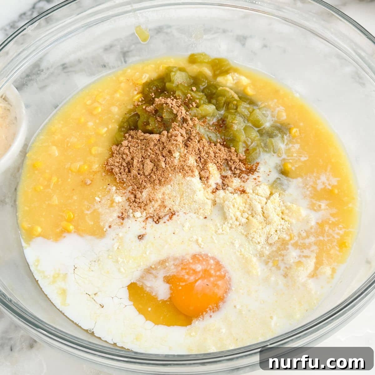 Fiesta Chicken Tamale Bake 4 A large mixing bowl containing egg, taco seasoning, milk, cream style corn, and diced green chiles.