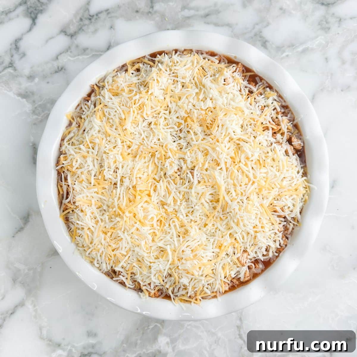 Fiesta Chicken Tamale Bake 8 A pie dish with layers of cornbread, enchilada sauce, and chicken, now generously topped with shredded cheese.