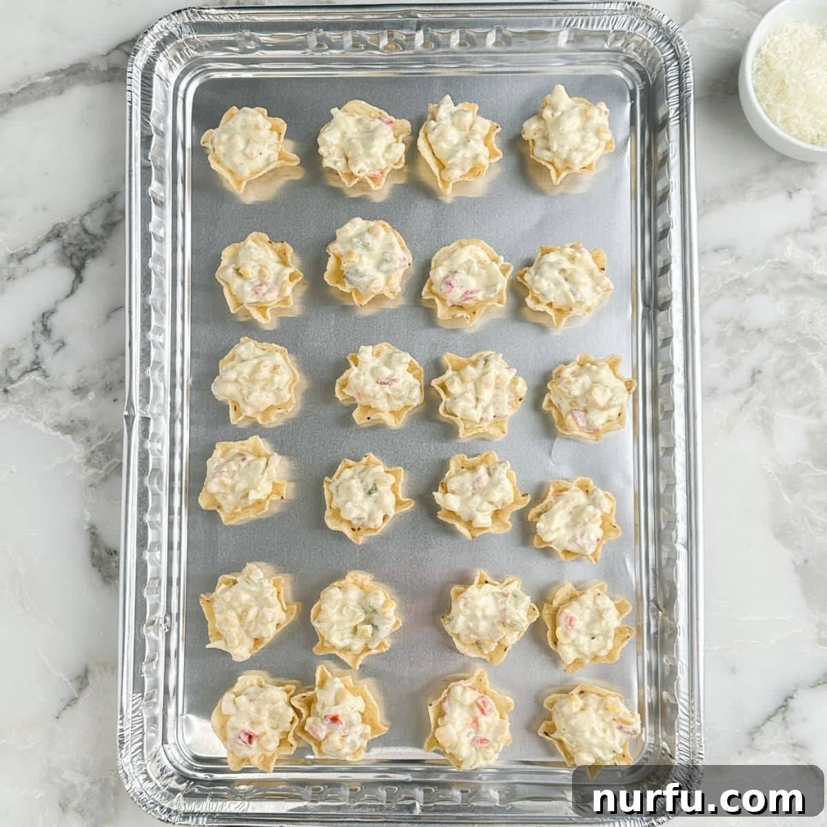 Hawkeye Hootenanny Bites 7 A baking pan filled with Tostitos Scoops, each generously topped with the Iowa Party Bite filling and sprinkled with Parmesan cheese, ready for the oven.