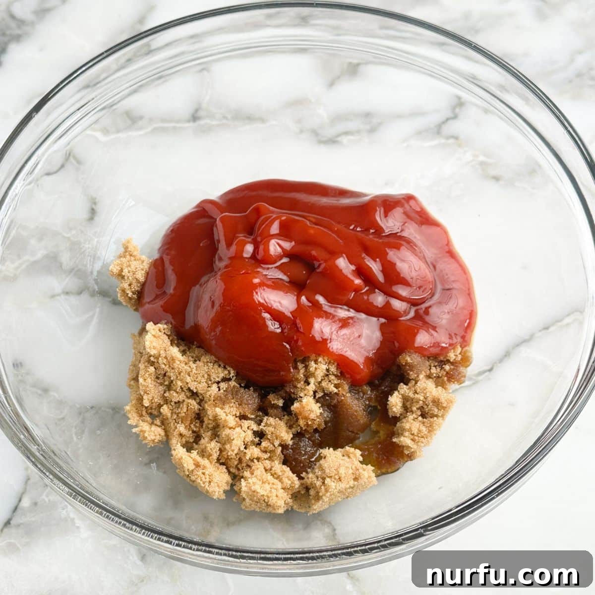 A mixing bowl containing light brown sugar and ketchup, with Worcestershire sauce nearby, ready to be combined for the glaze.
