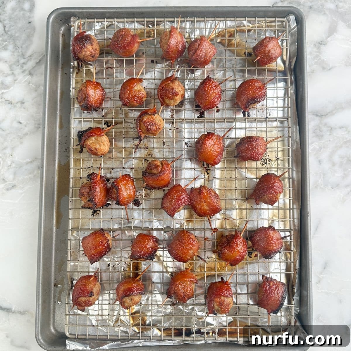 Close-up of baked bacon wrapped meatballs on a wire rack, glistening with the sweet and savory glaze, perfectly caramelized.