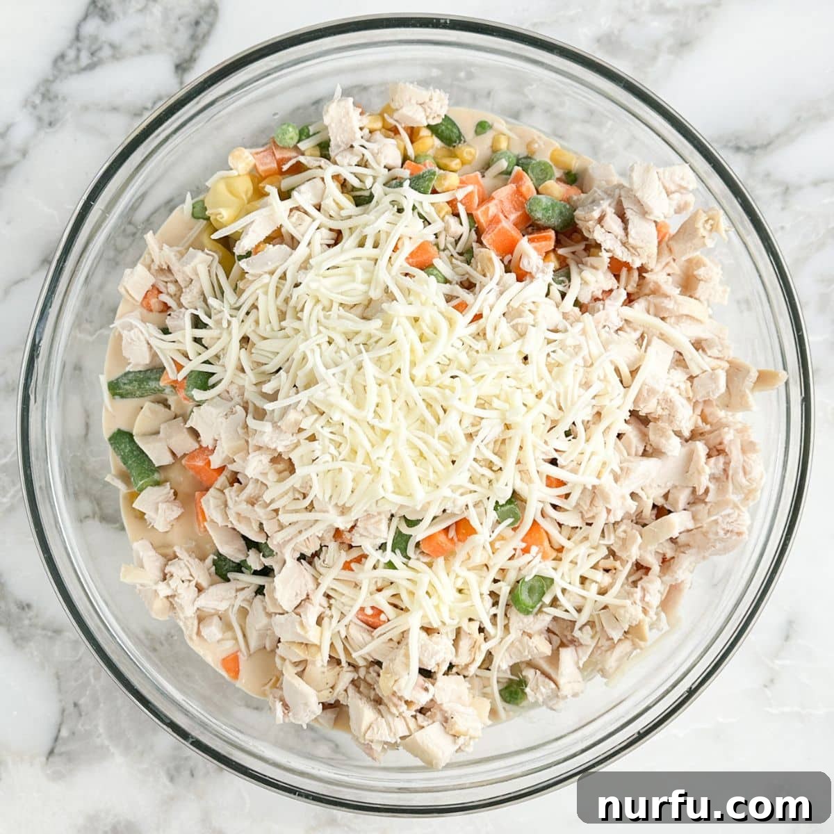 Bowl of shredded chicken, tortellini, alfredo sauce, vegetables, and shredded cheese. 