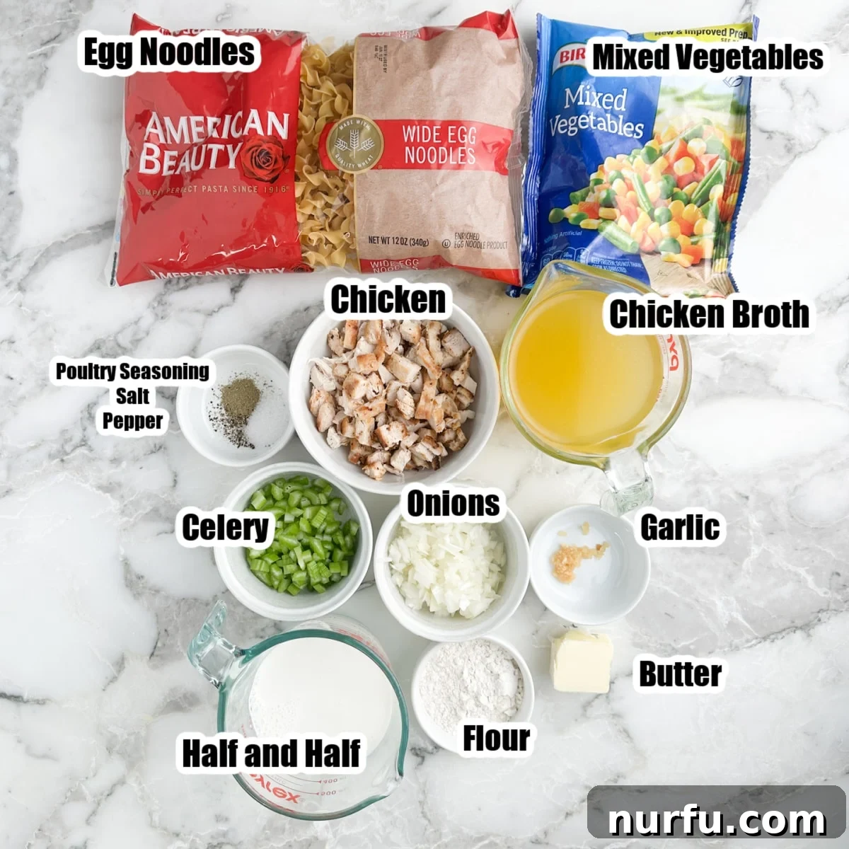 Hearty Chicken Pot Pie Pasta 3 A flat lay of ingredients for chicken pot pie pasta, including a bag of egg noodles, a bowl of shredded chicken, a bag of frozen mixed vegetables, chicken broth, half and half, butter, diced celery, diced onion, a garlic clove, and a small dish of seasonings.