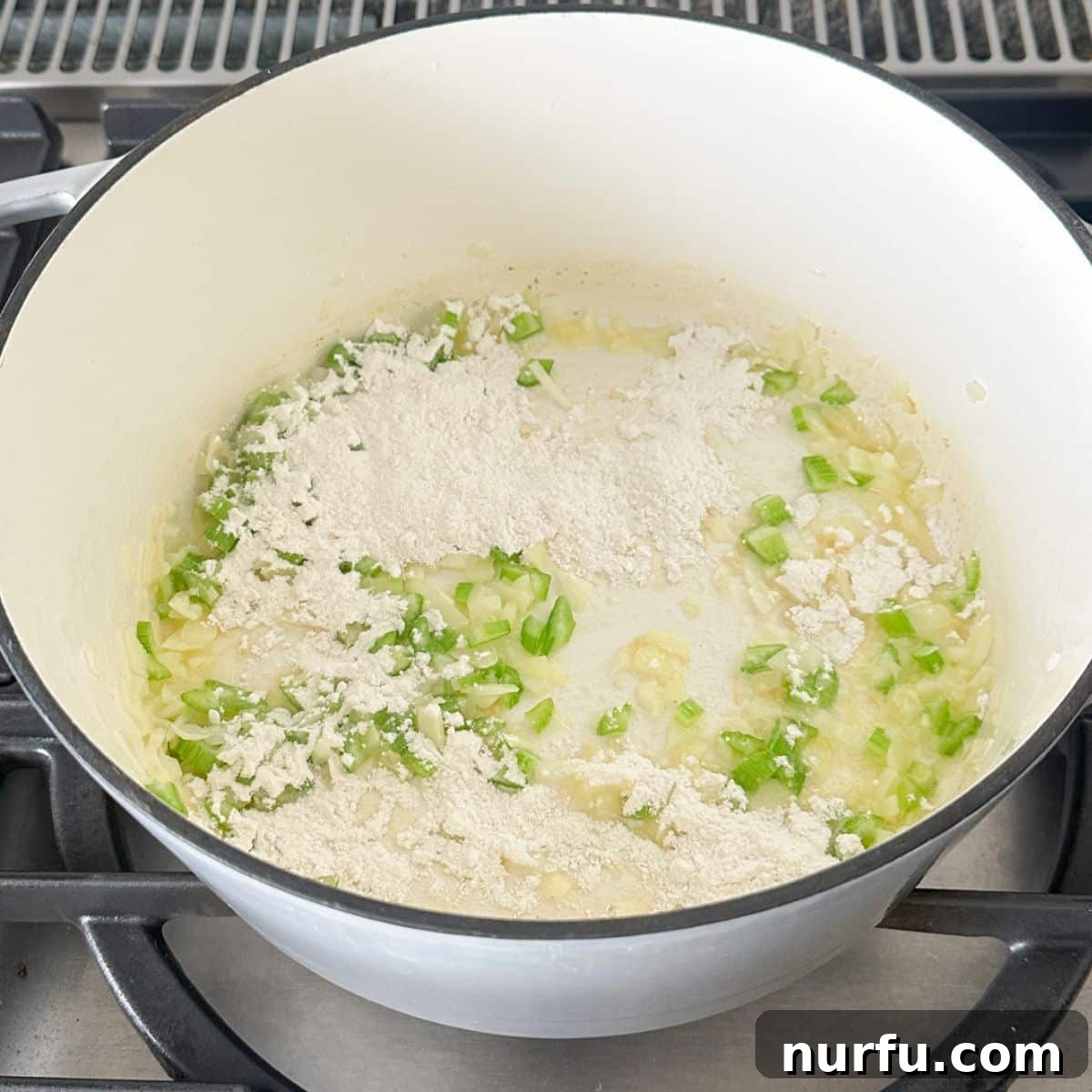 Hearty Chicken Pot Pie Pasta 5 A close-up view of a pot containing sautéed onion and celery with flour just added, being whisked together to create a roux for the creamy sauce.