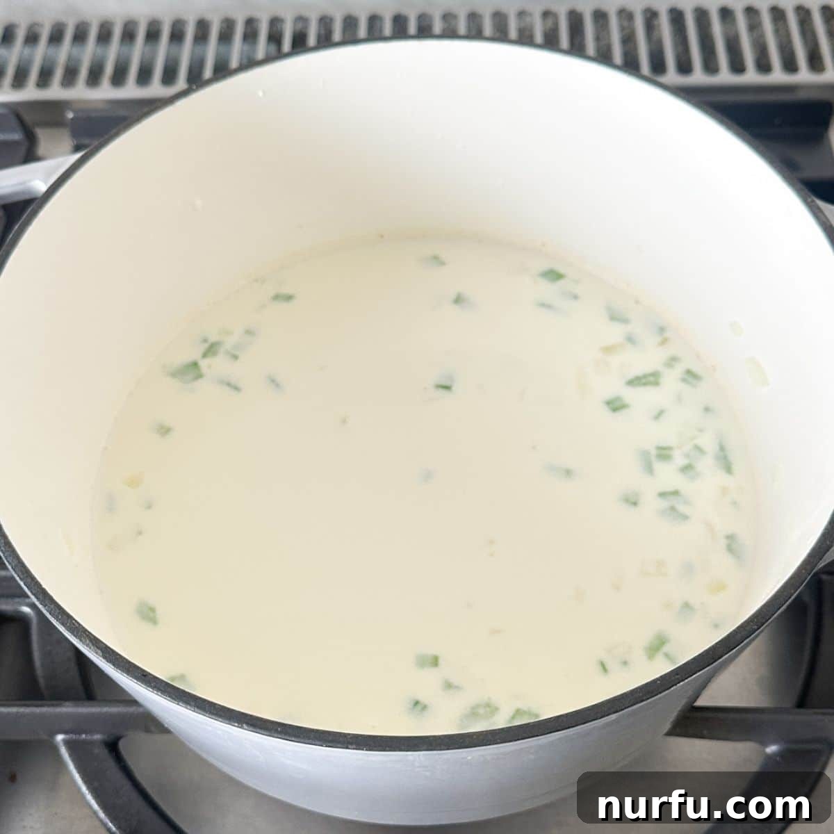 Hearty Chicken Pot Pie Pasta 6 A pot on the stove with a creamy white sauce simmering, indicating that the broth, half and half, and seasonings have been added and are thickening.