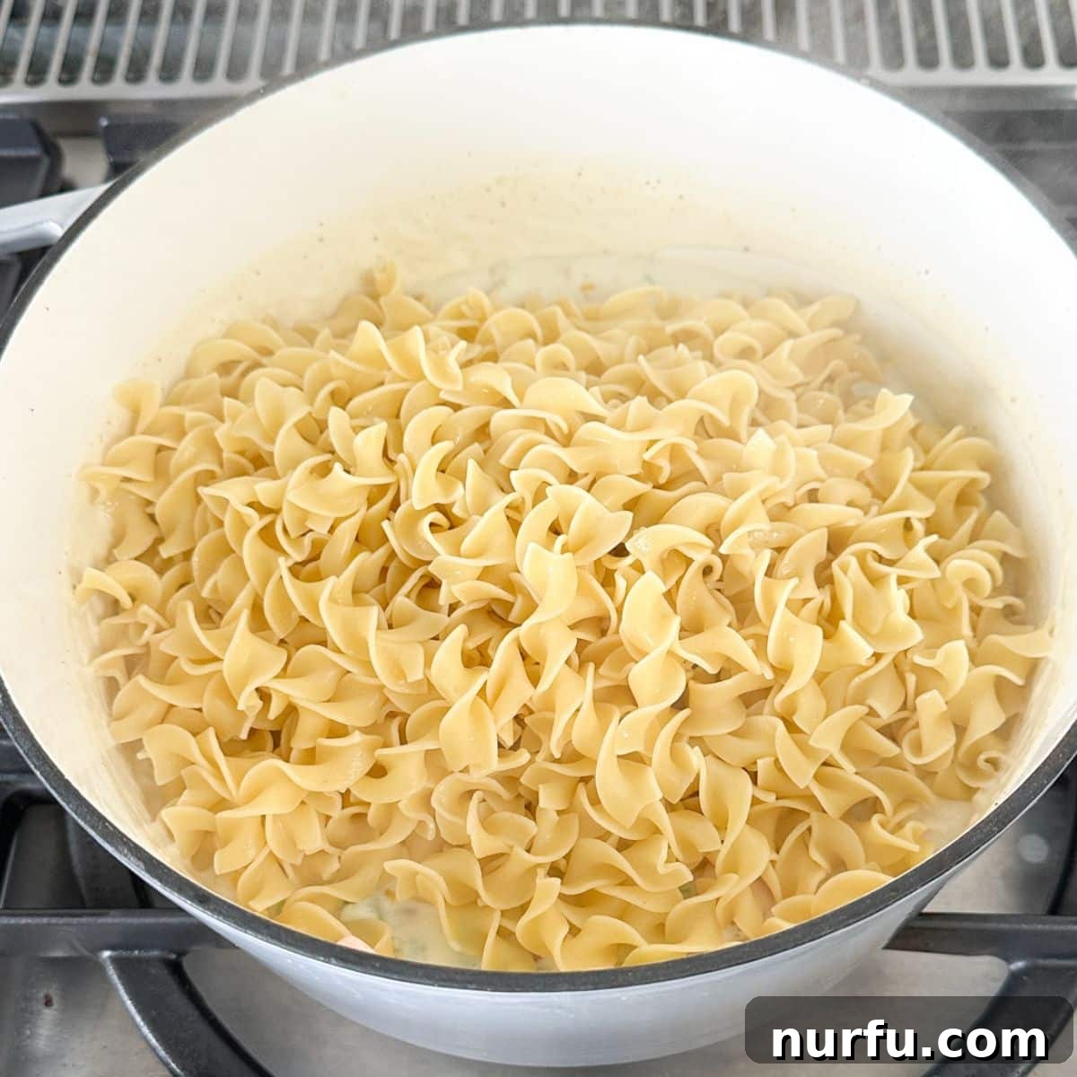 Hearty Chicken Pot Pie Pasta 8 A large pot of creamy chicken pot pie sauce with cooked egg noodles being added and mixed in thoroughly, ready to serve.