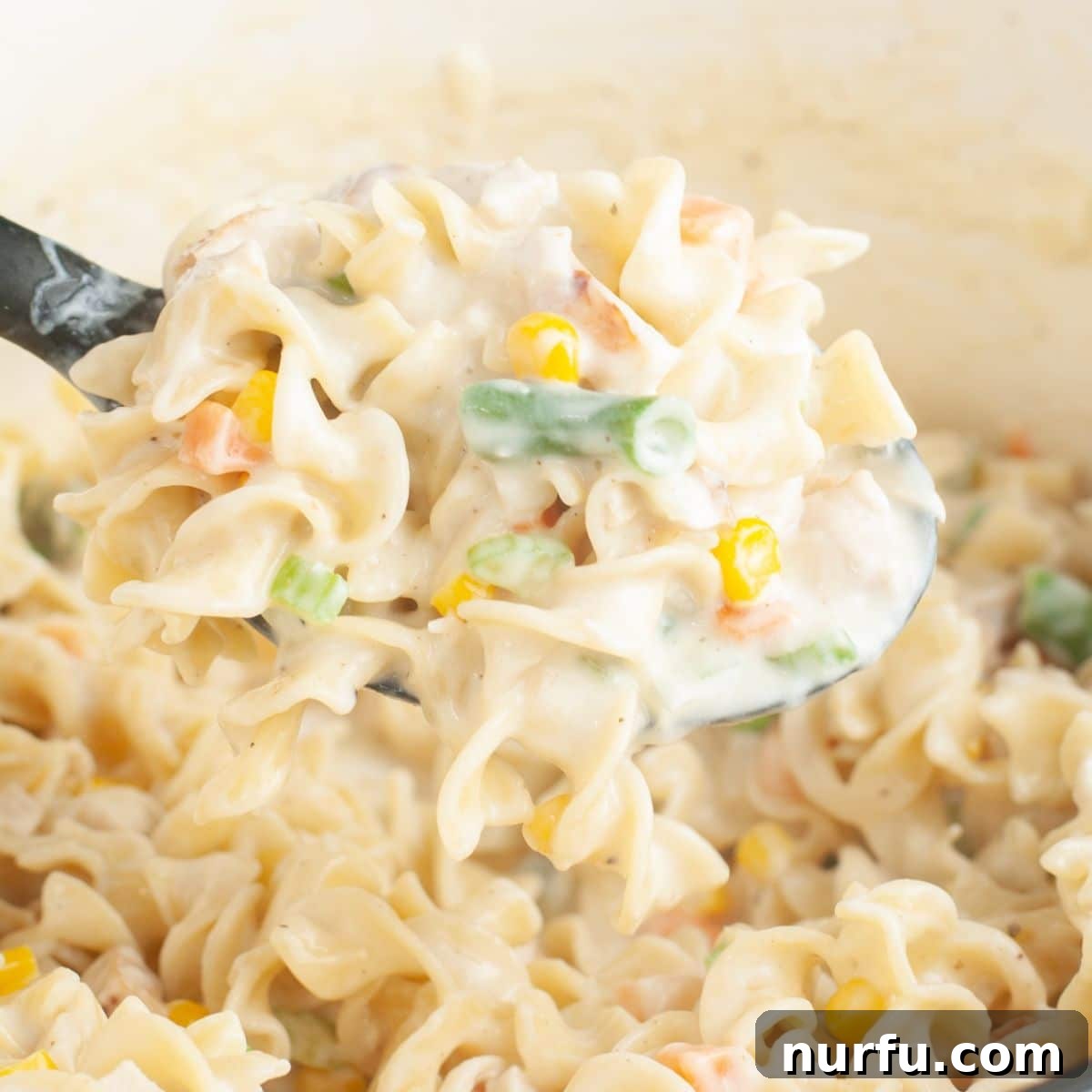 Hearty Chicken Pot Pie Pasta 9 A generous serving of chicken pot pie pasta on a spoon, lifted from the pot, showcasing the creamy sauce, tender chicken, and mixed vegetables.
