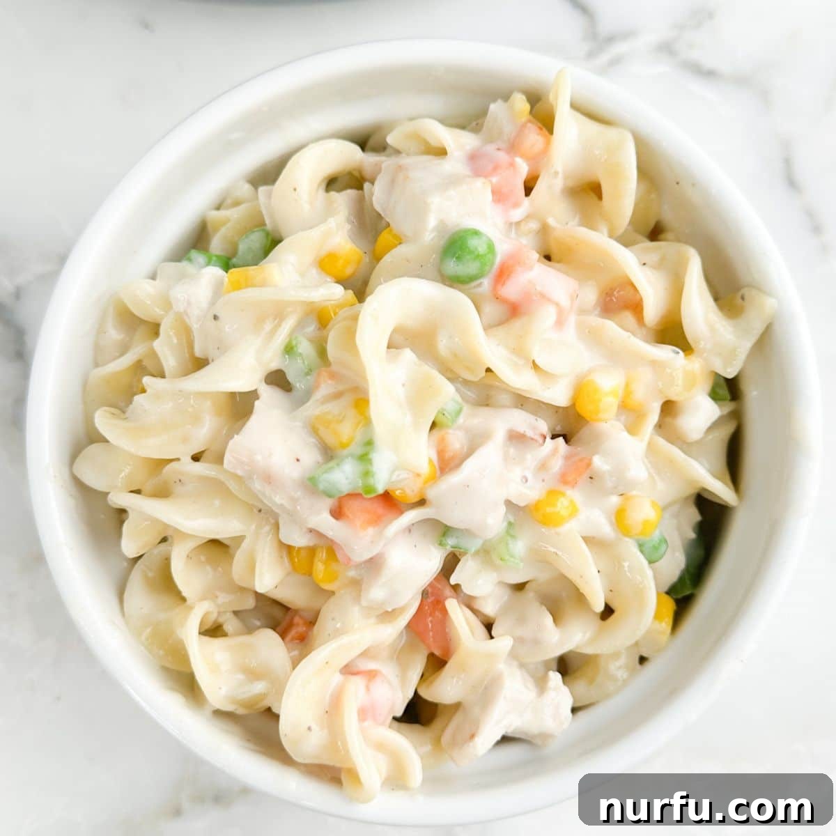 Hearty Chicken Pot Pie Pasta 10 A bowl filled with creamy chicken pot pie pasta, showcasing a rich, savory sauce, tender shredded chicken, and colorful mixed vegetables.