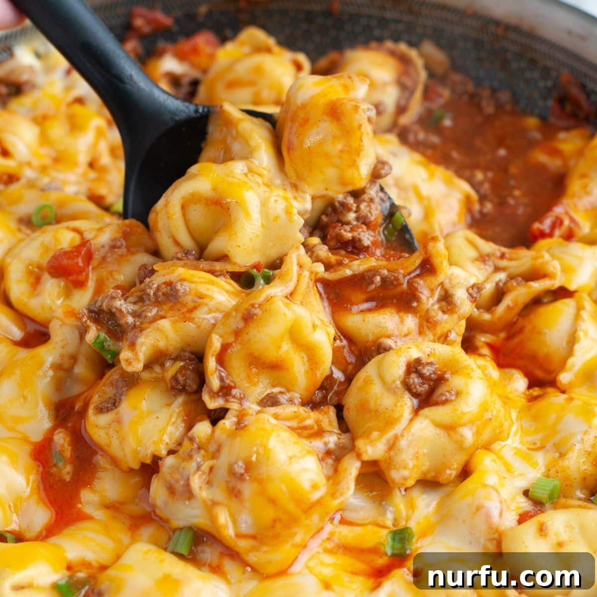 Fiesta Tortellini 2 A close-up shot of a spoon lifting a scoop of cheesy taco tortellini from a skillet, showcasing melted cheese and seasoned beef. A perfect illustration of the hearty and delicious one-pot meal.