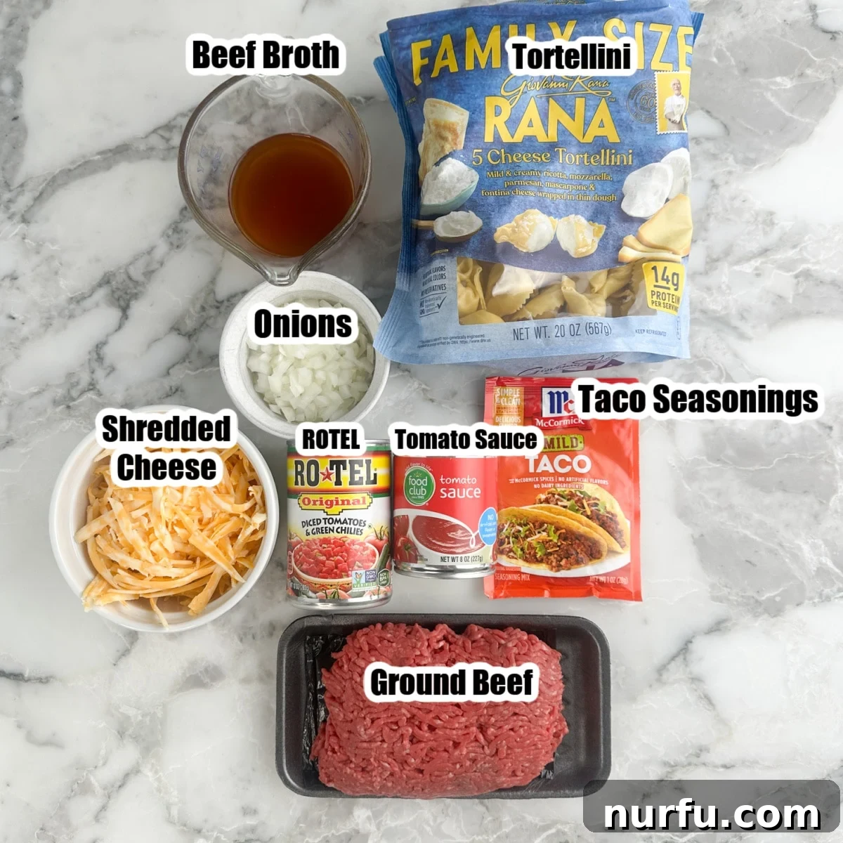 Fiesta Tortellini 3 A flat lay photograph showcasing all the fresh ingredients for taco tortellini: ground beef, refrigerated tortellini, shredded cheese, beef broth, diced onions, a packet of taco seasoning, a can of Rotel, and a can of tomato sauce.