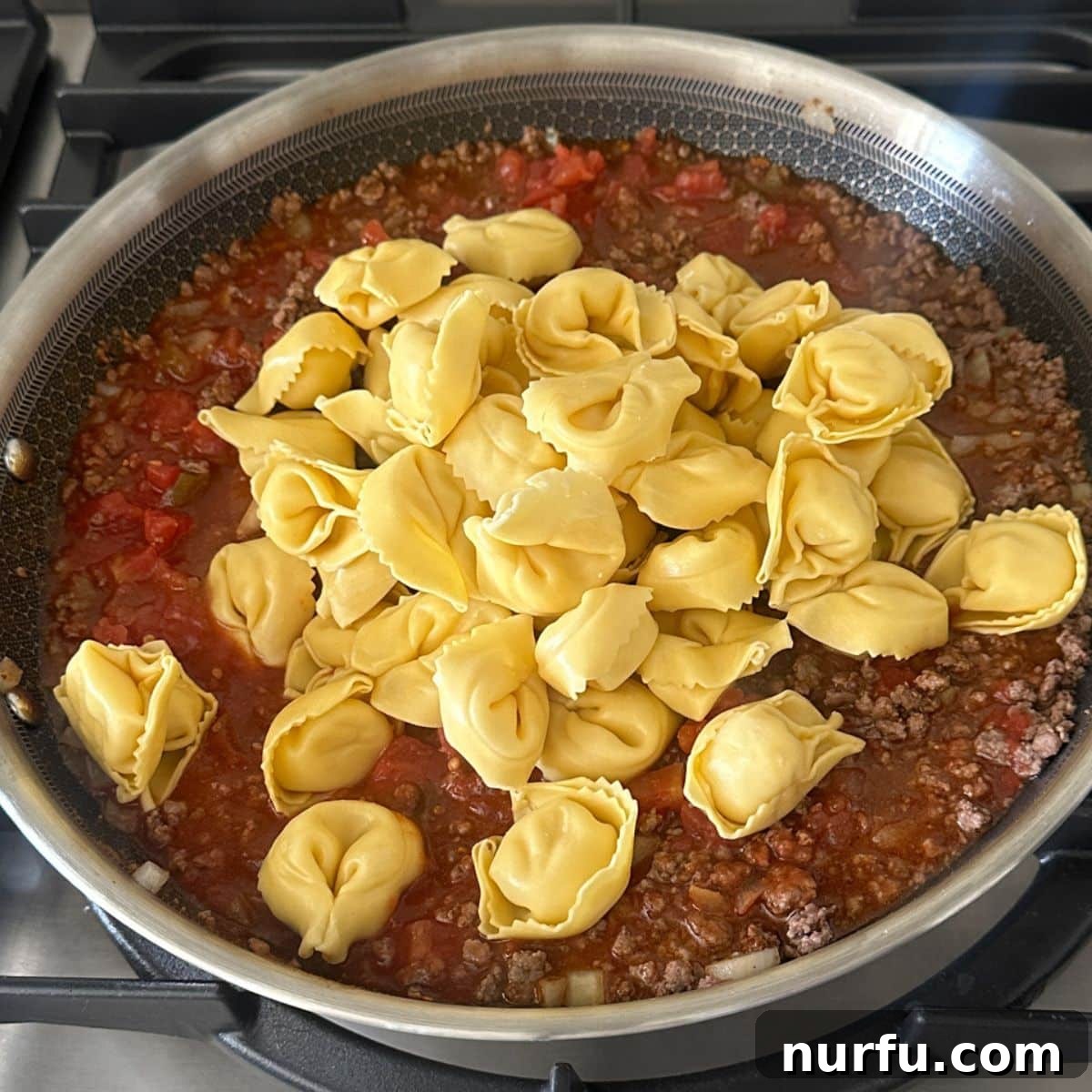 Fiesta Tortellini 7 Refrigerated tortellini being stirred into the simmering ground beef and tomato sauce mixture in a skillet.