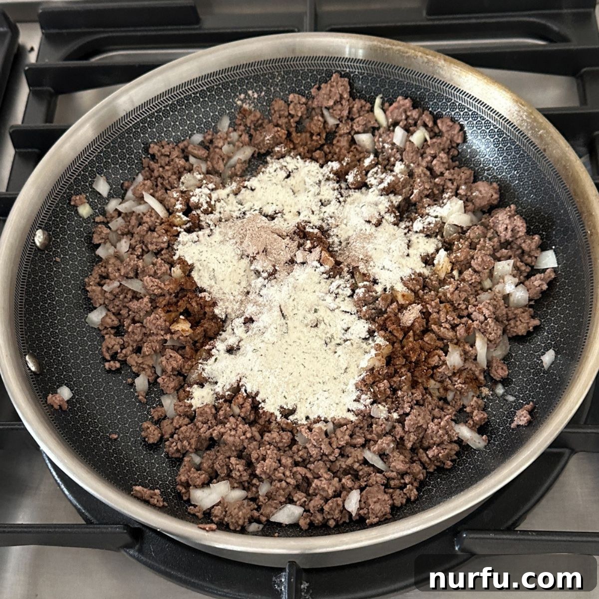 Mississippi Roadhouse Sloppy Joes 5 Skillet with ground beef, diced onions, and ranch seasoning being stirred in.