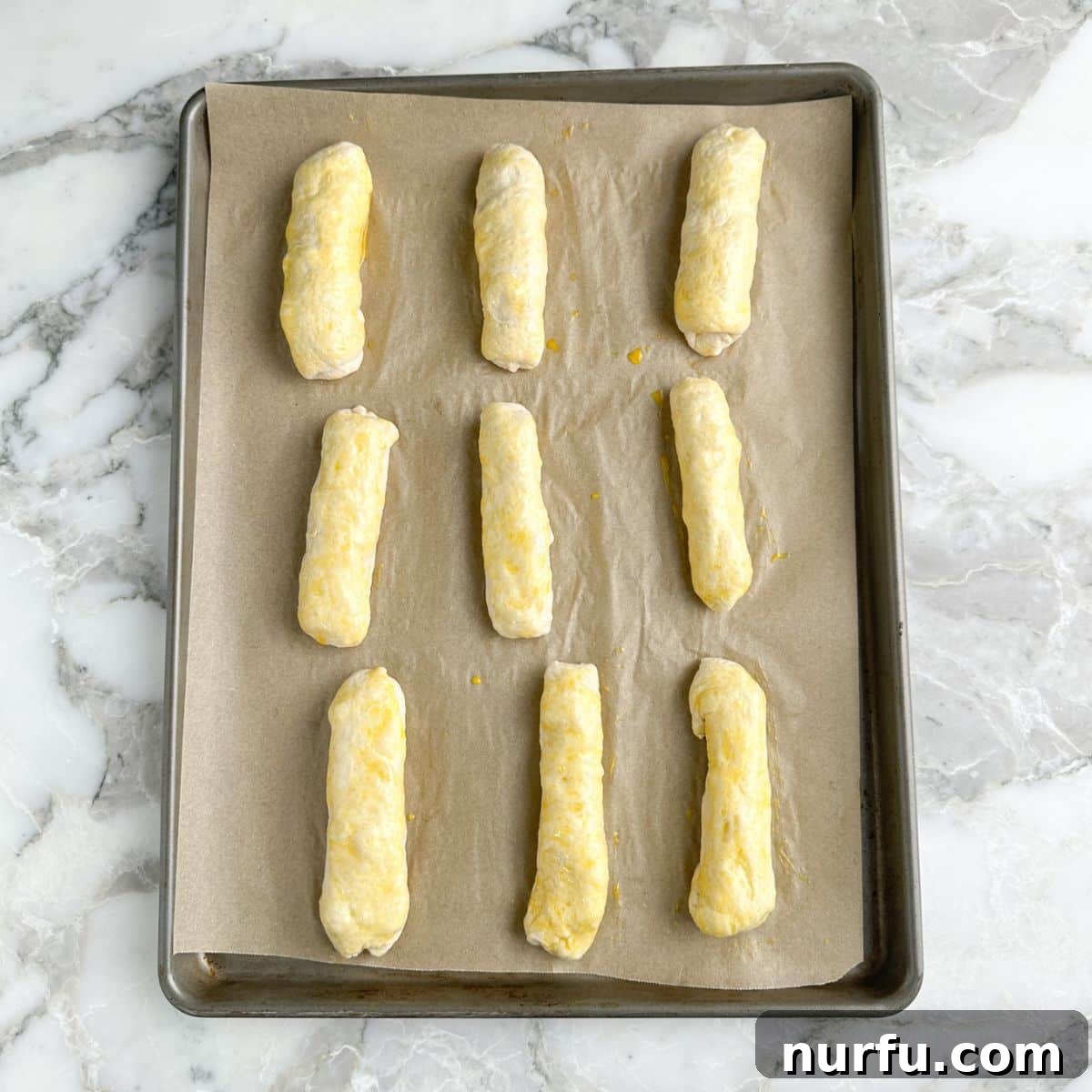 Cheesy Pepperoni Rolls 7 Uncooked pepperoni rolls on a baking pan, now brushed with a golden egg wash, ready to be baked.