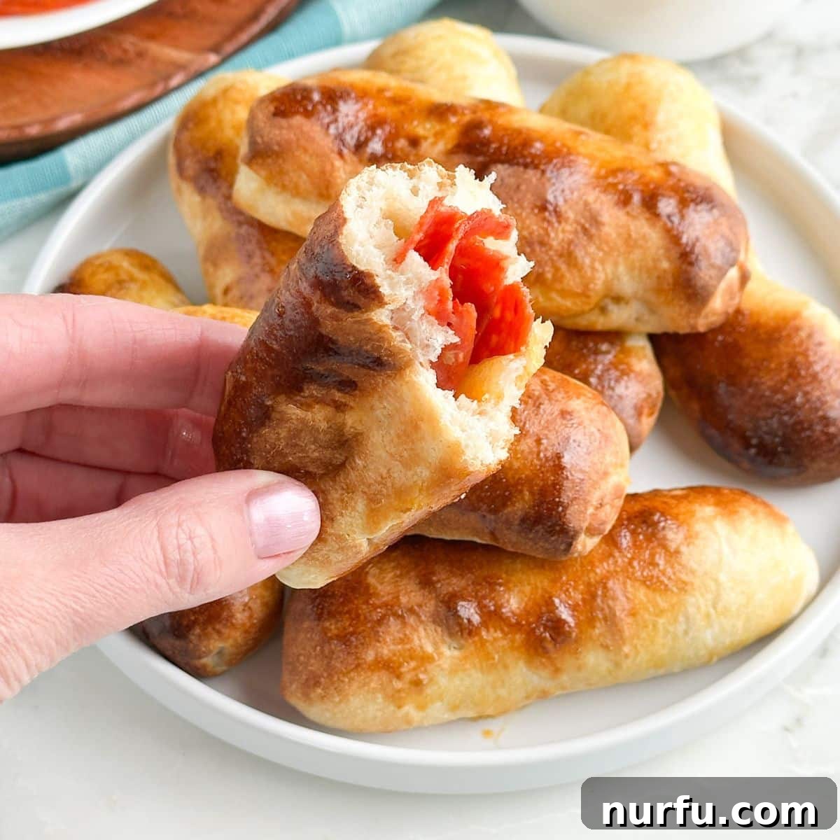 Cheesy Pepperoni Rolls 8 A hand holding a perfectly baked, golden-brown pepperoni roll, showcasing its soft texture and the melted cheese and pepperoni peeking out.