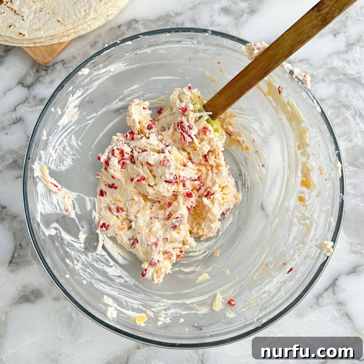 A bowl of creamy pimento cheese mixture with a spatula, showcasing its smooth texture.