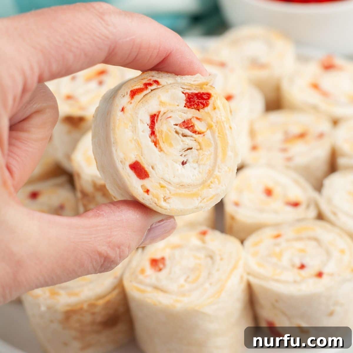 A hand holding a perfectly sliced pimento cheese pinwheel, showing the creamy filling and tight roll.
