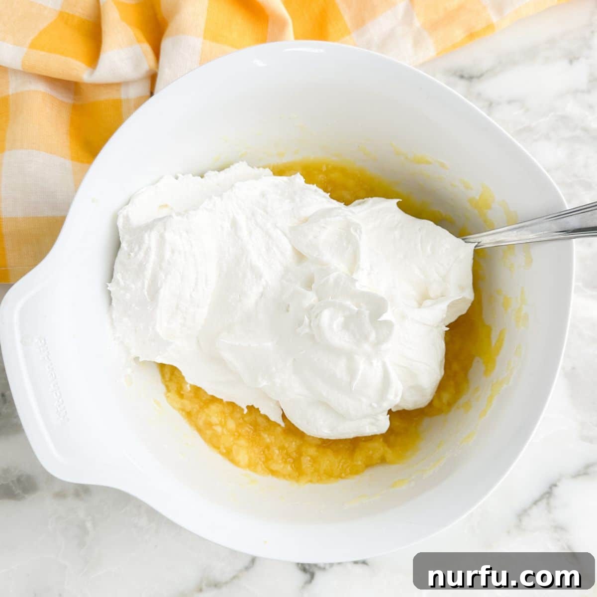 The crushed pineapple and whipped topping are gently folded together in a bowl, creating the base for the no-bake Lemon Fluff.