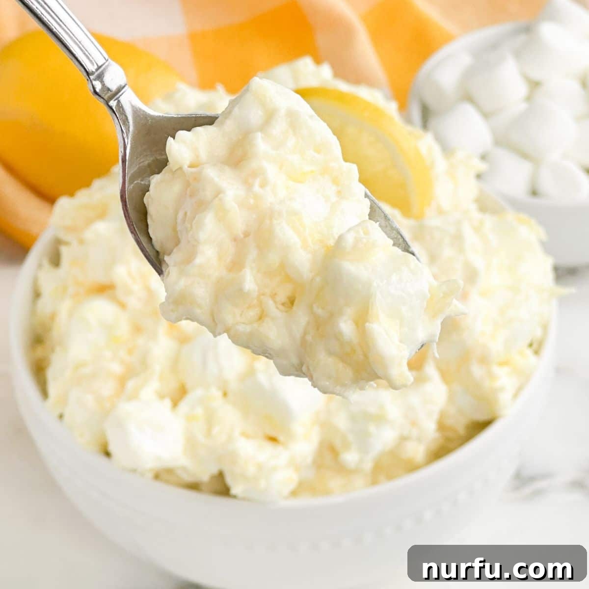 A spoon scooping a portion of light and creamy Lemon Fluff from a bowl, highlighting its perfect texture.
