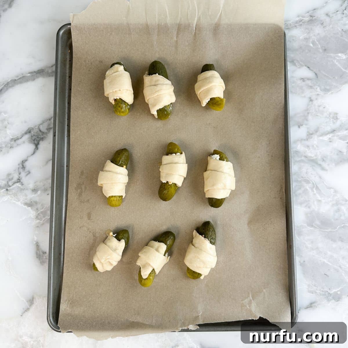 Tangy Pickle Bites 6 A baking pan filled with unbaked pickles in a blanket, neatly arranged on parchment paper.