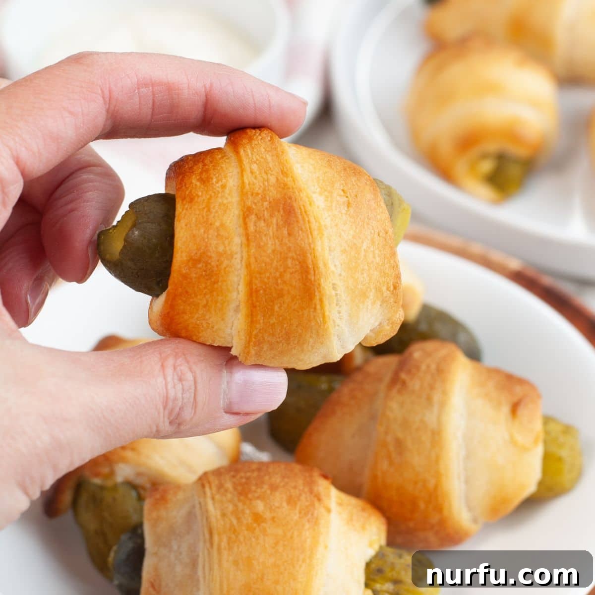 Tangy Pickle Bites 9 A hand holding a single, perfectly golden-brown pickle in a blanket, showcasing its inviting appearance.