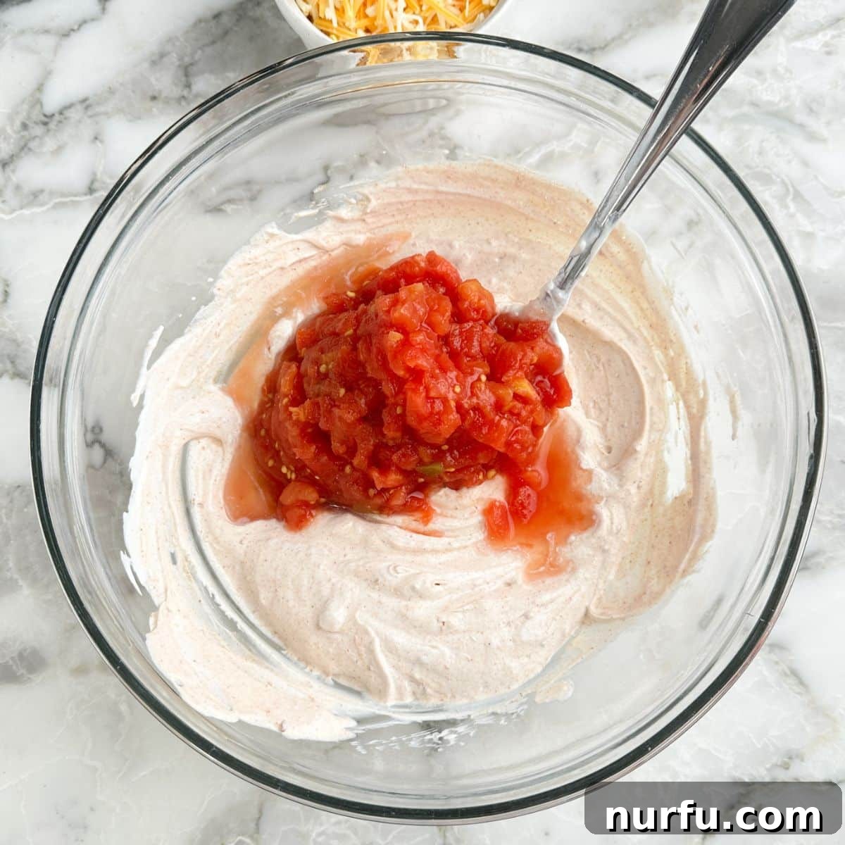 Zesty Fiesta Ranch Dip 6 A bowl of ranch dip base with ROTEL diced tomatoes and green chilies being added.