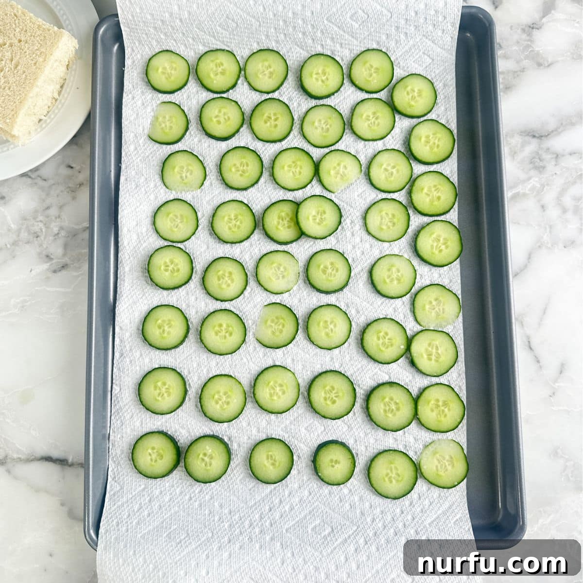 Elegant Cucumber Tea Bites 6 Baking pan with a paper towel and thinly sliced cucumbers, patted dry.