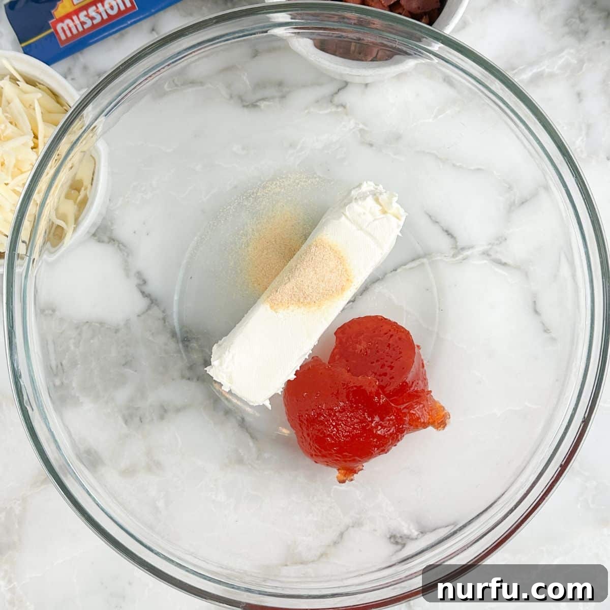 Sweet Heat Pinwheels 4 A bowl containing a creamy mixture of softened cream cheese, garlic powder, and vibrant red pepper jelly, ready to be blended.