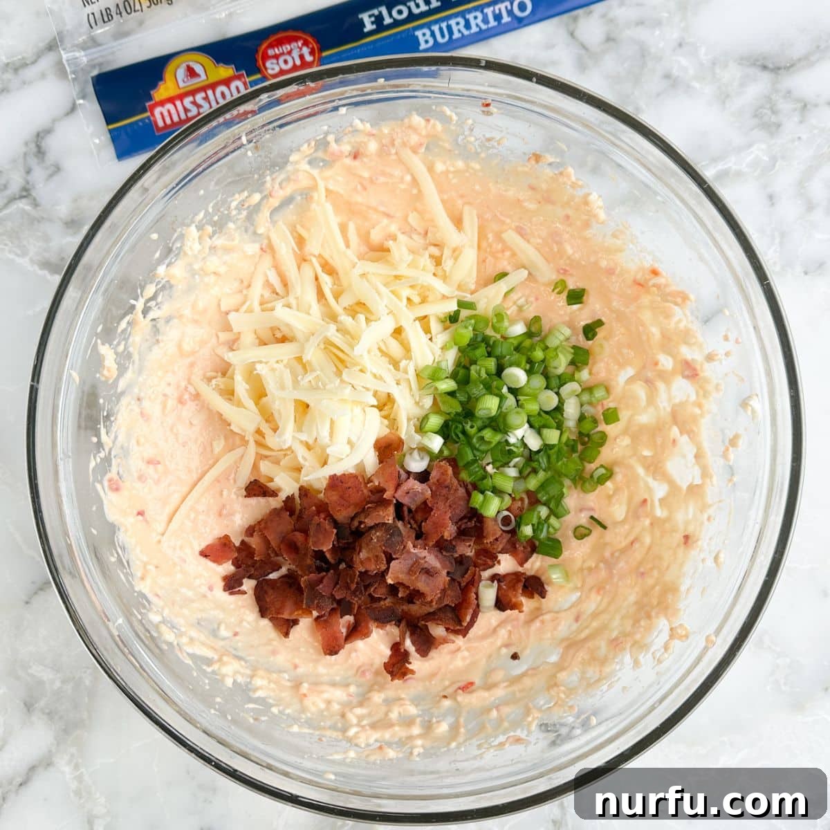 Sweet Heat Pinwheels 5 A bowl filled with the complete pepper jelly mixture, showing shredded cheese, crispy bacon bits, and chopped green onions stirred in.