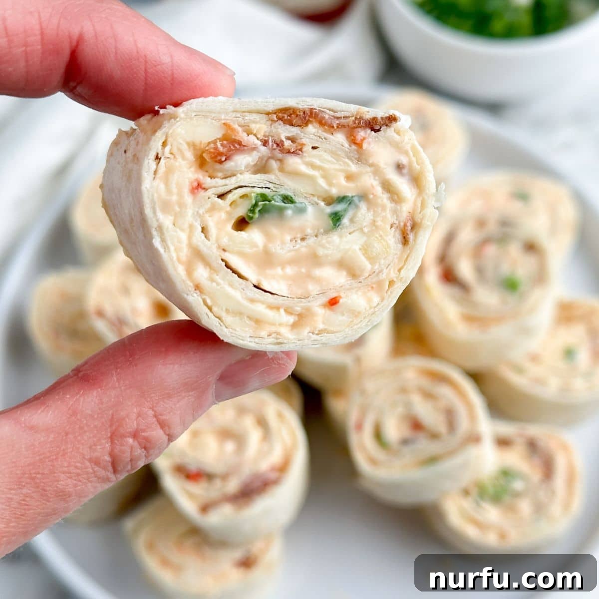 Sweet Heat Pinwheels 9 A hand holds a single perfectly sliced pepper jelly pinwheel, showcasing its colorful swirl and inviting texture.