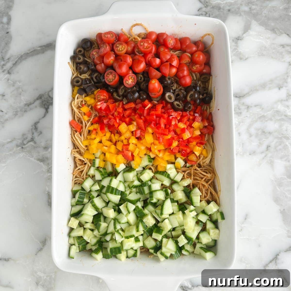 Zesty Spaghetti Salad 7 Casserole dish with diced cucumbers, diced peppers, olives, and tomatoes.