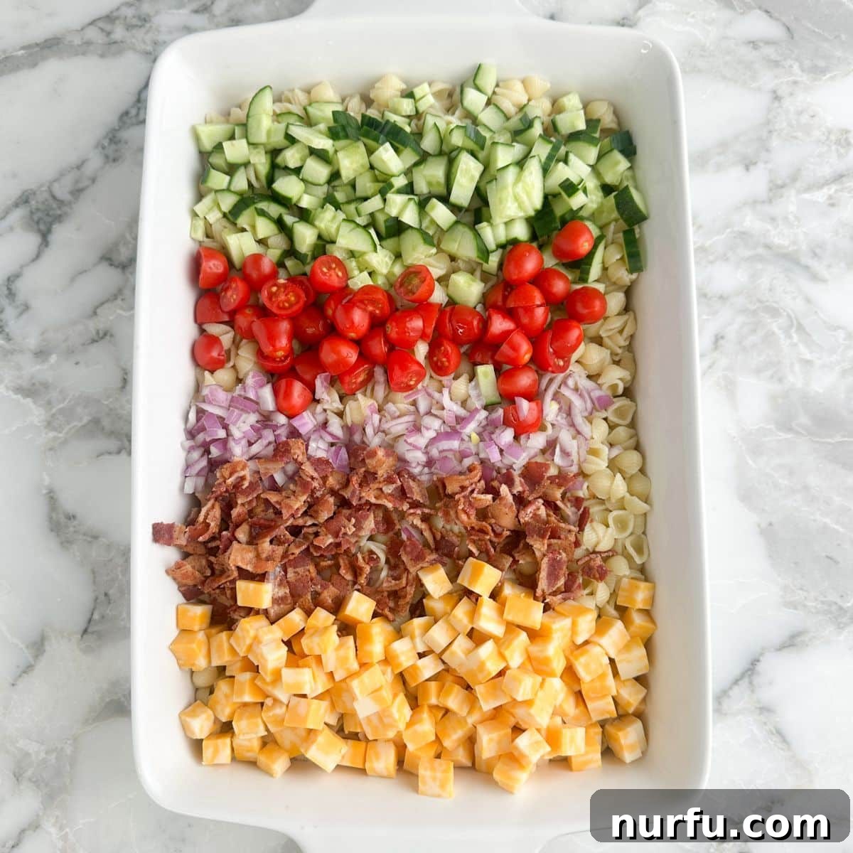 Creamy Ranch Pasta Salad Recipe with Bacon and Veggies 4 Casserole dish with pasta, diced cucumbers, tomatoes, onion, bacon crumbles, and cubed cheese.