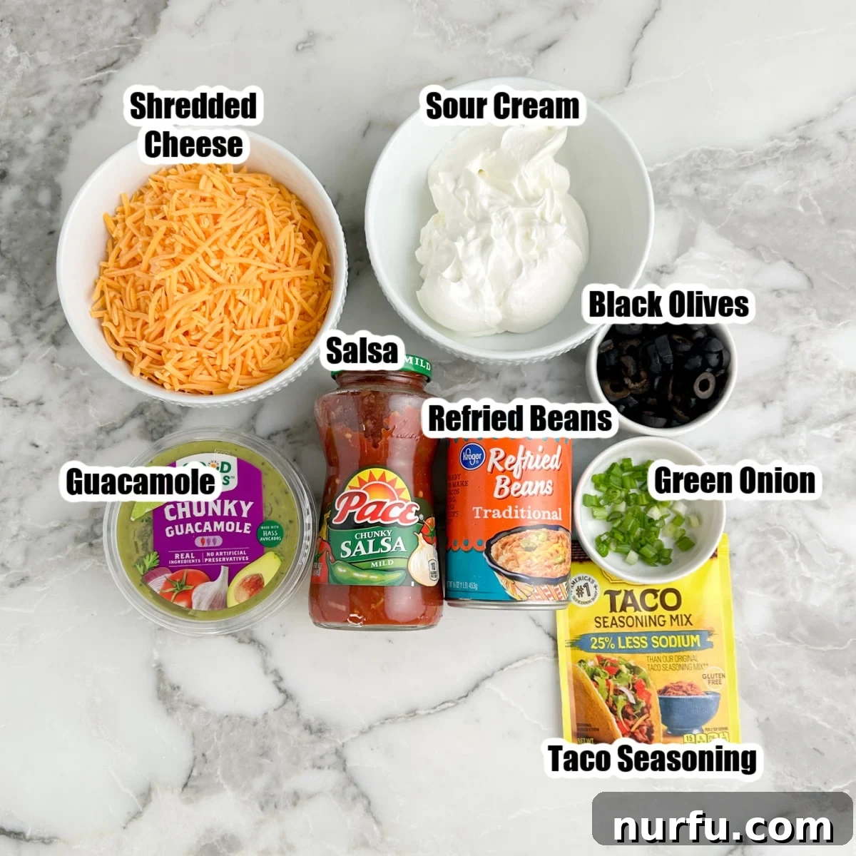 Creamy 5-Layer Dip Recipe for Parties and Game Day 3 Bowl of shredded cheese, sour cream, salsa, guacamole, beans, taco seasonings, olives, and green onions.