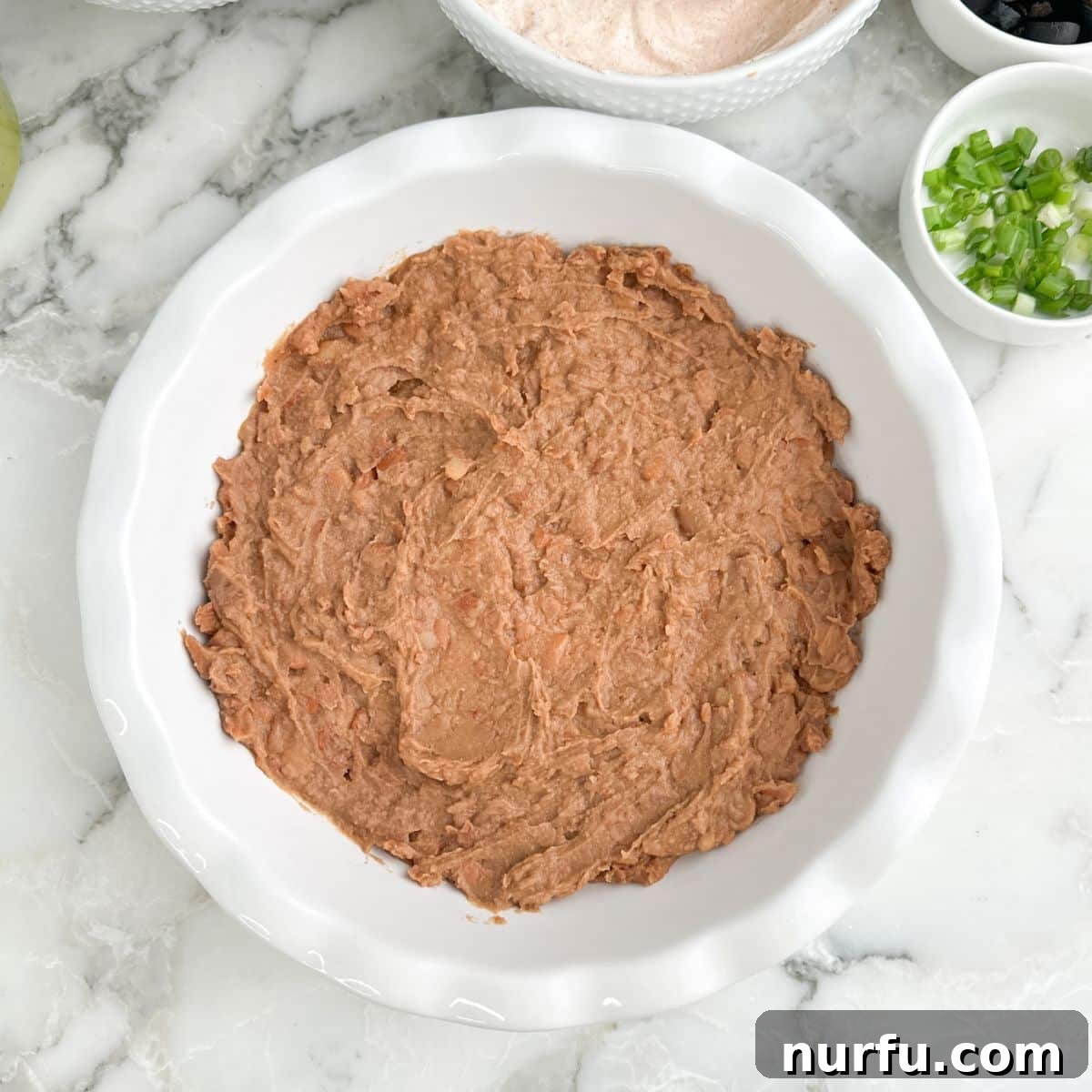 Creamy 5-Layer Dip Recipe for Parties and Game Day 5 Refried beans spread in a pie dish.
