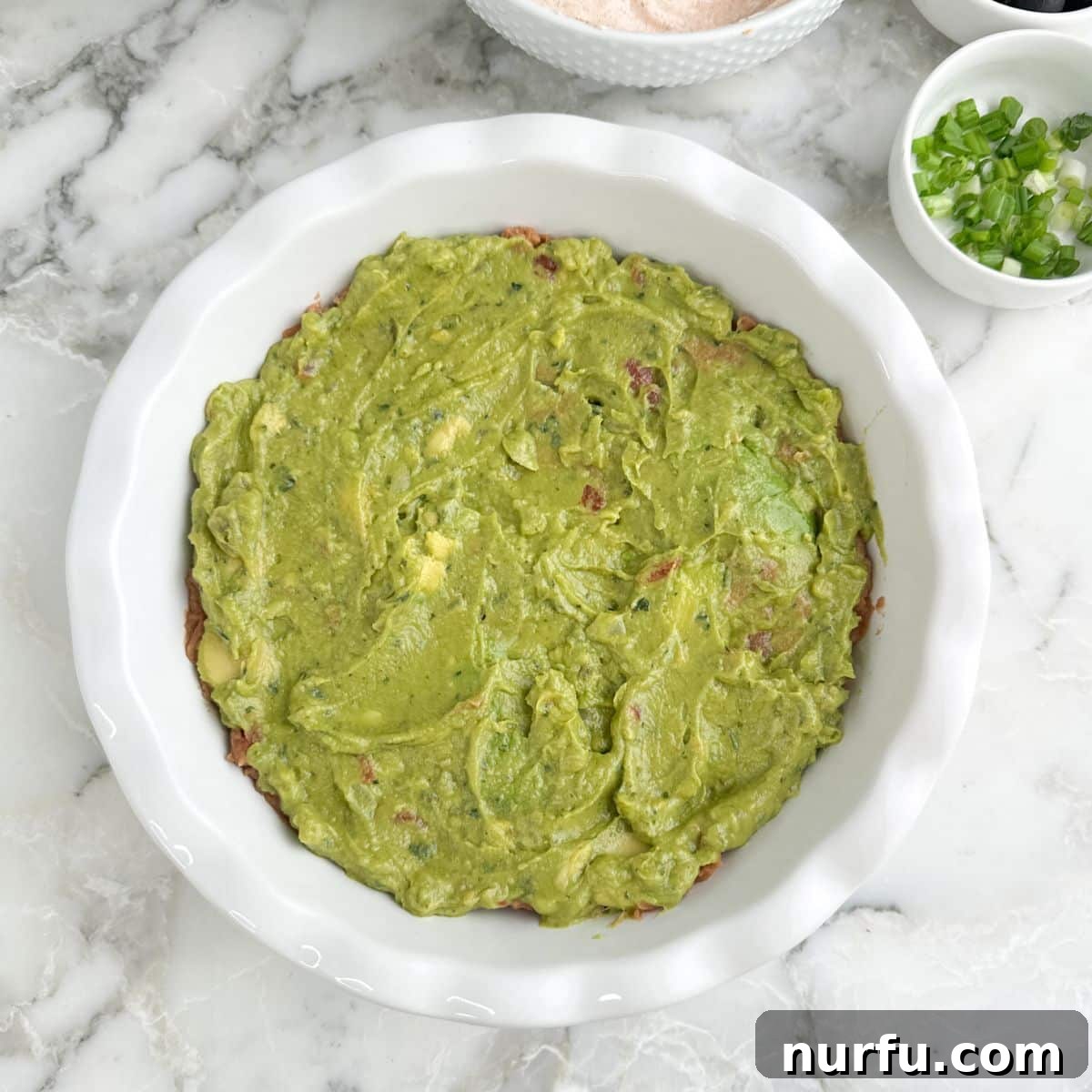 Creamy 5-Layer Dip Recipe for Parties and Game Day 6 Pie dish with guacamole spread out.