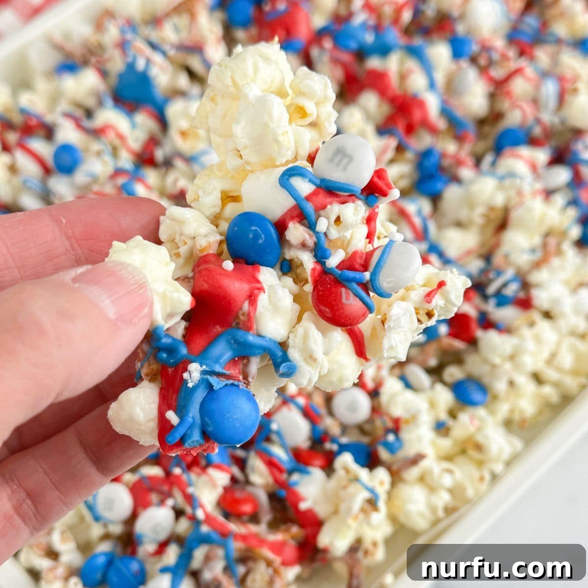 Patriotic Red, White & Blue Popcorn Snack Mix Recipe 5 Hand holding red white and blue popcorn snack mix.