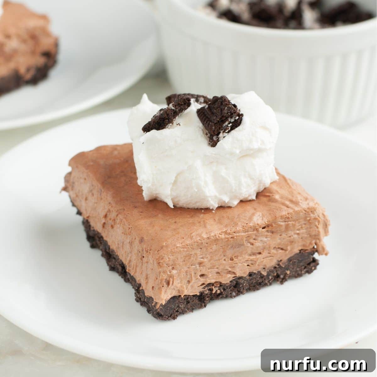 Piece of no bake chocolate pie topped with whipped cream and crumbled Oreo cookies.