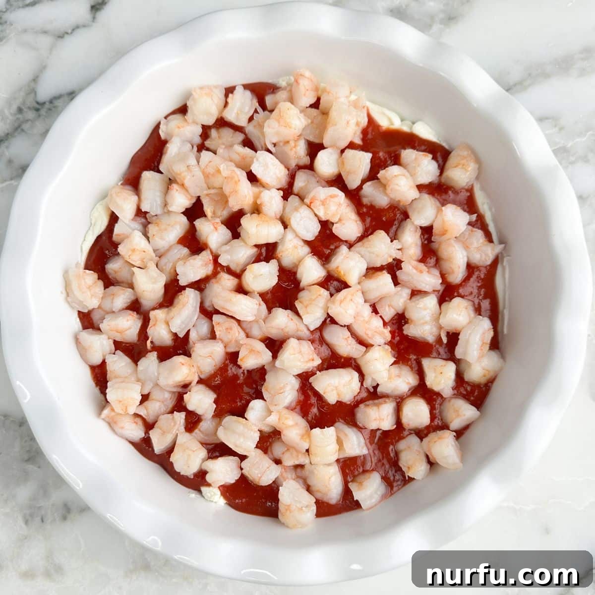 Baking dish with cocktail sauce and shrimp.