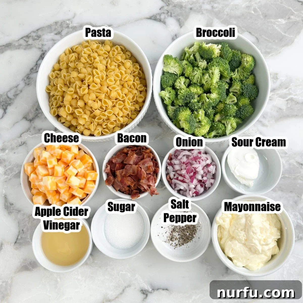 Bowl of pasta, broccoli, cubed cheese, bacon, onions, sour cream, mayonnaise, vinegar, sugar, salt, and pepper.