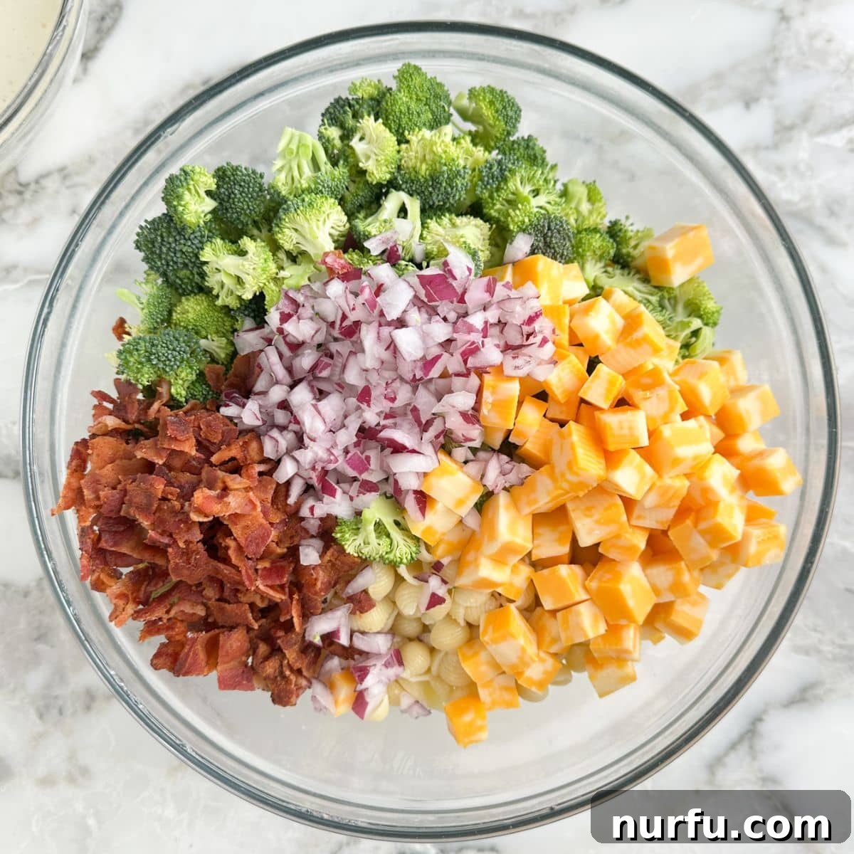 Bowl with pasta, bacon, broccoli, cheese, and red onion.