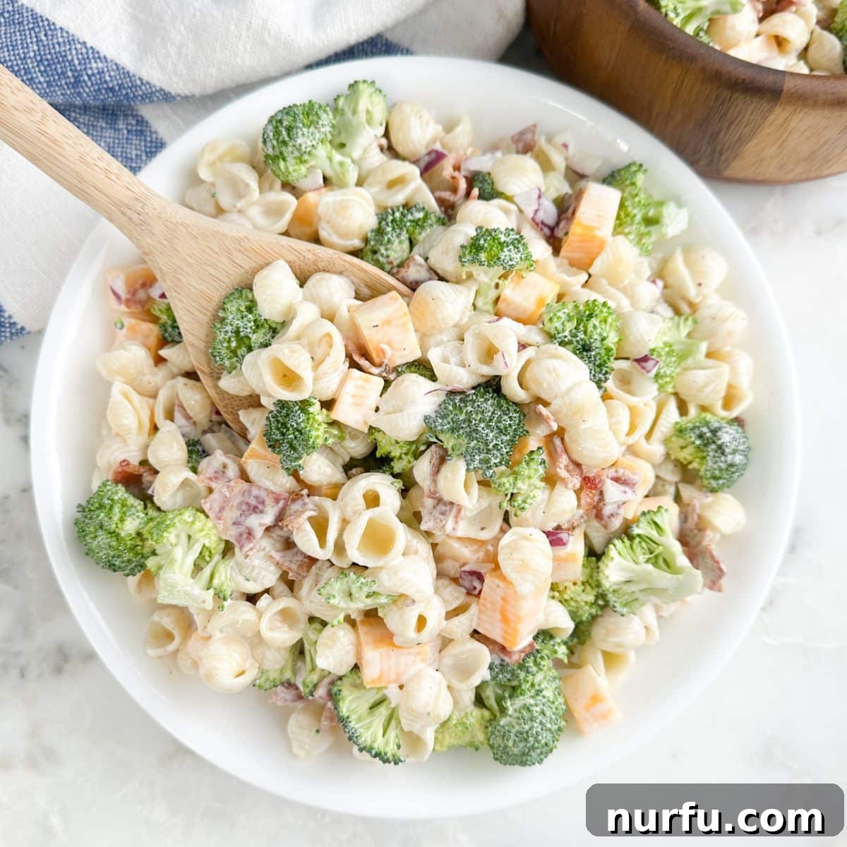 Bowl of broccoli pasta salad with a wooden spoon.
