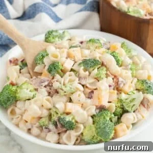 Bowl filled with broccoli pasta salad and wooden spoon.