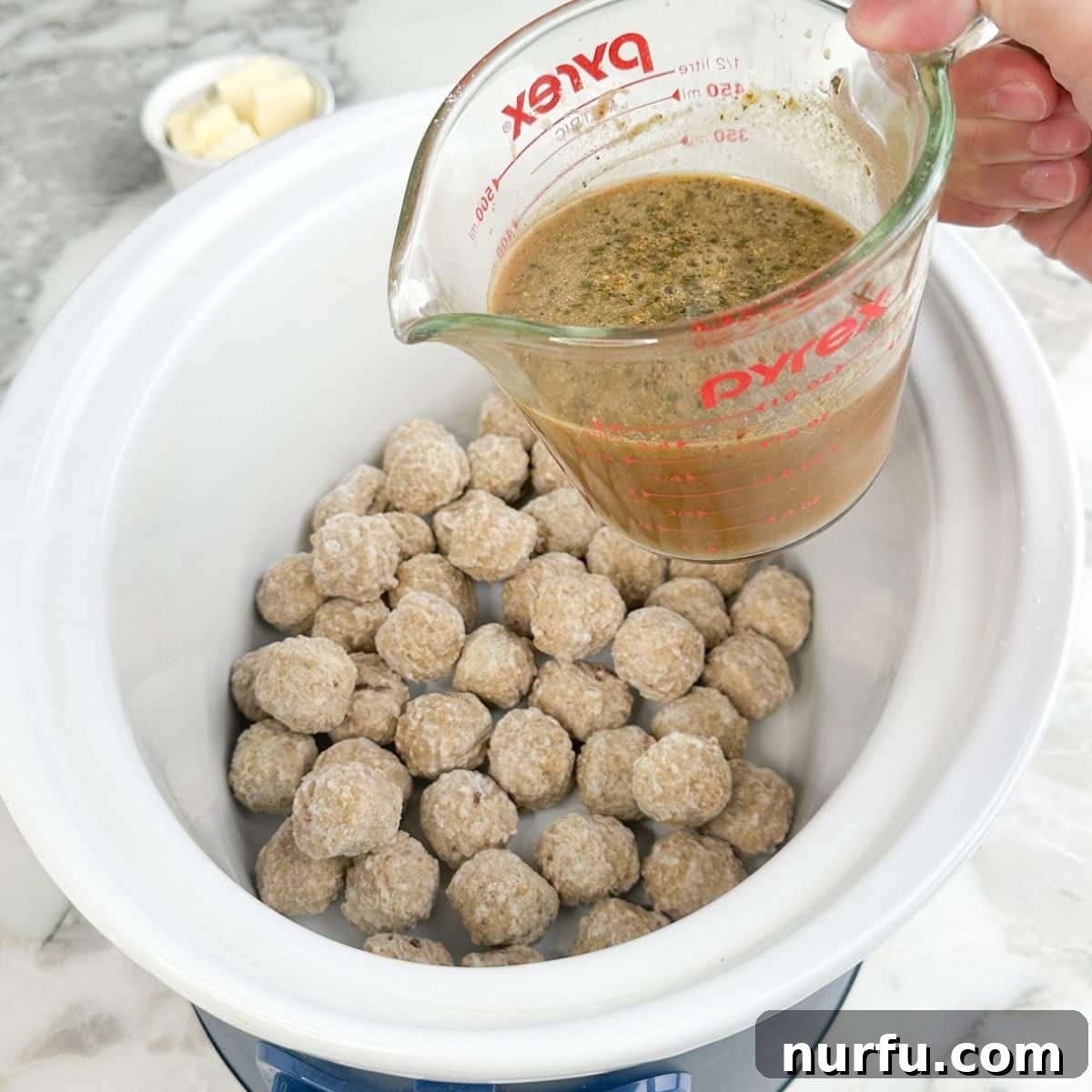 Classic Mississippi Meatballs with Tangy Pepperoncini Sauce 5 Frozen meatballs in a slow cooker with broth in a measuring cup.