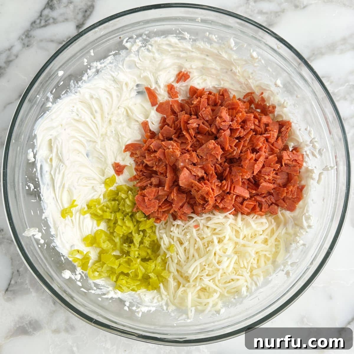 Bowl with whipped cream cheese, chopped pepperoni, mozzarella cheese, and chopped peperoncini peppers.